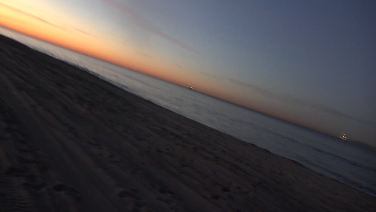 Low waves on a tilted shoreline under a blue-orange dusk sky.