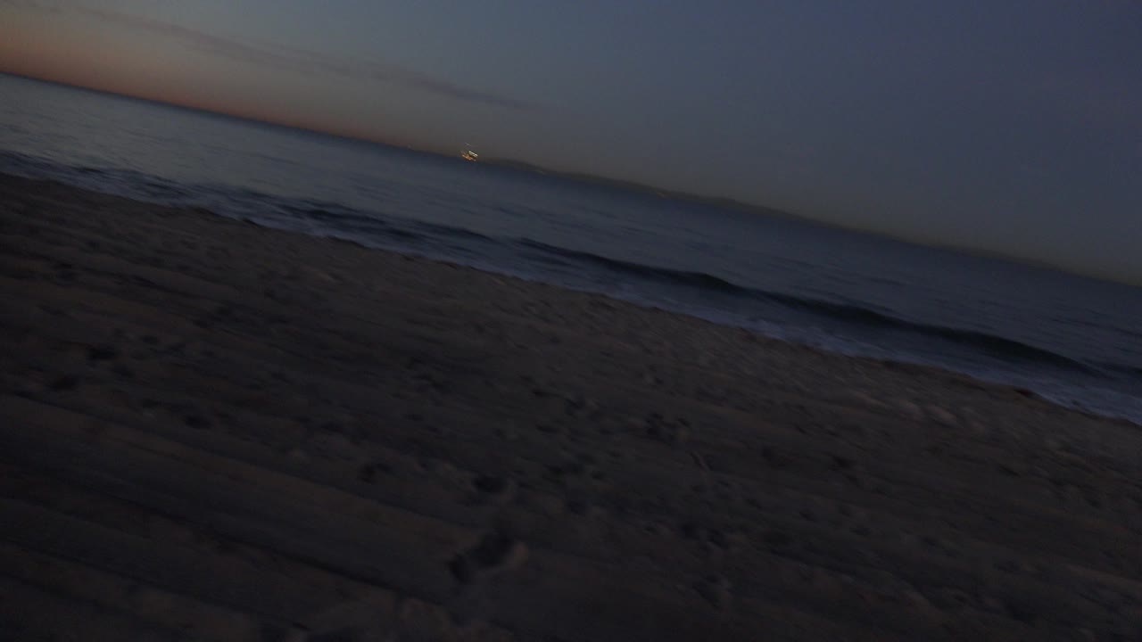 Dark sandy beach and ocean waves with a slanted horizon.