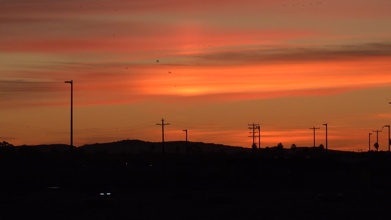 At 0:00, a reddish sunset sky over Huntington Beach sits above a dark roadside horizon with utility poles, faint headlights, and no visible people.