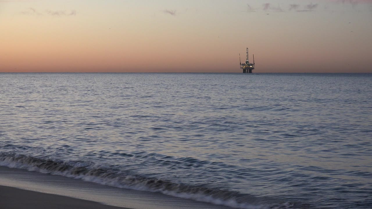 Distant offshore vessel beyond small waves at sunset