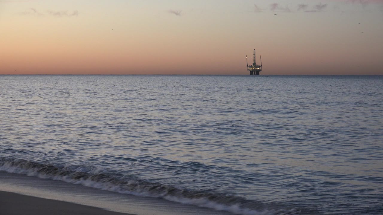 A shore break rolls closer in the foreground while the distant vessel remains on the Huntington Beach horizon, with no visible people.