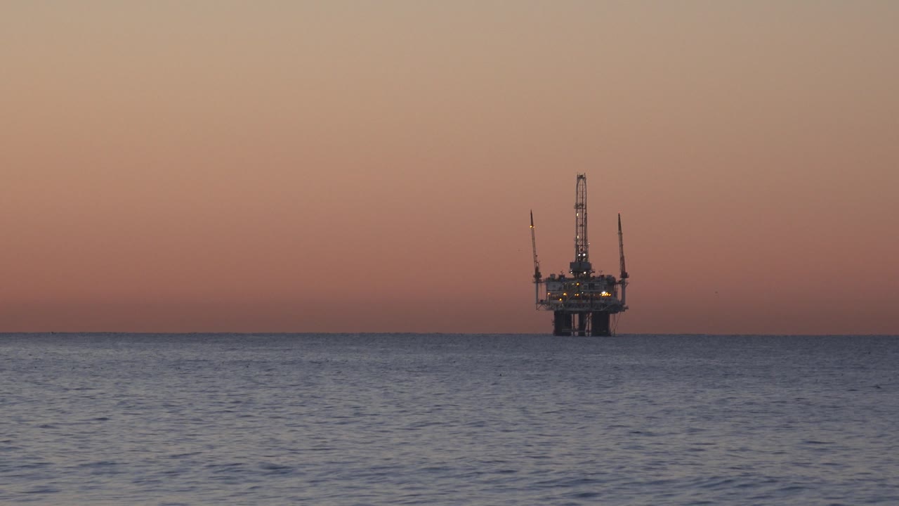 Distant offshore platform against a fading sunset sky.