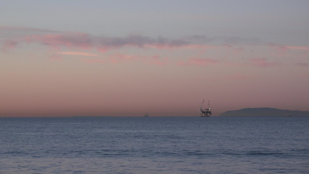 Oil rig near horizon with island silhouette at sundown