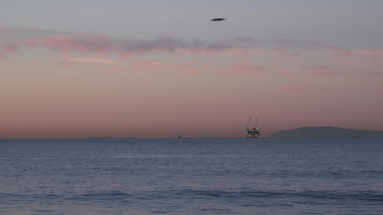 Ocean and sunset sky with platform near distant island shape.