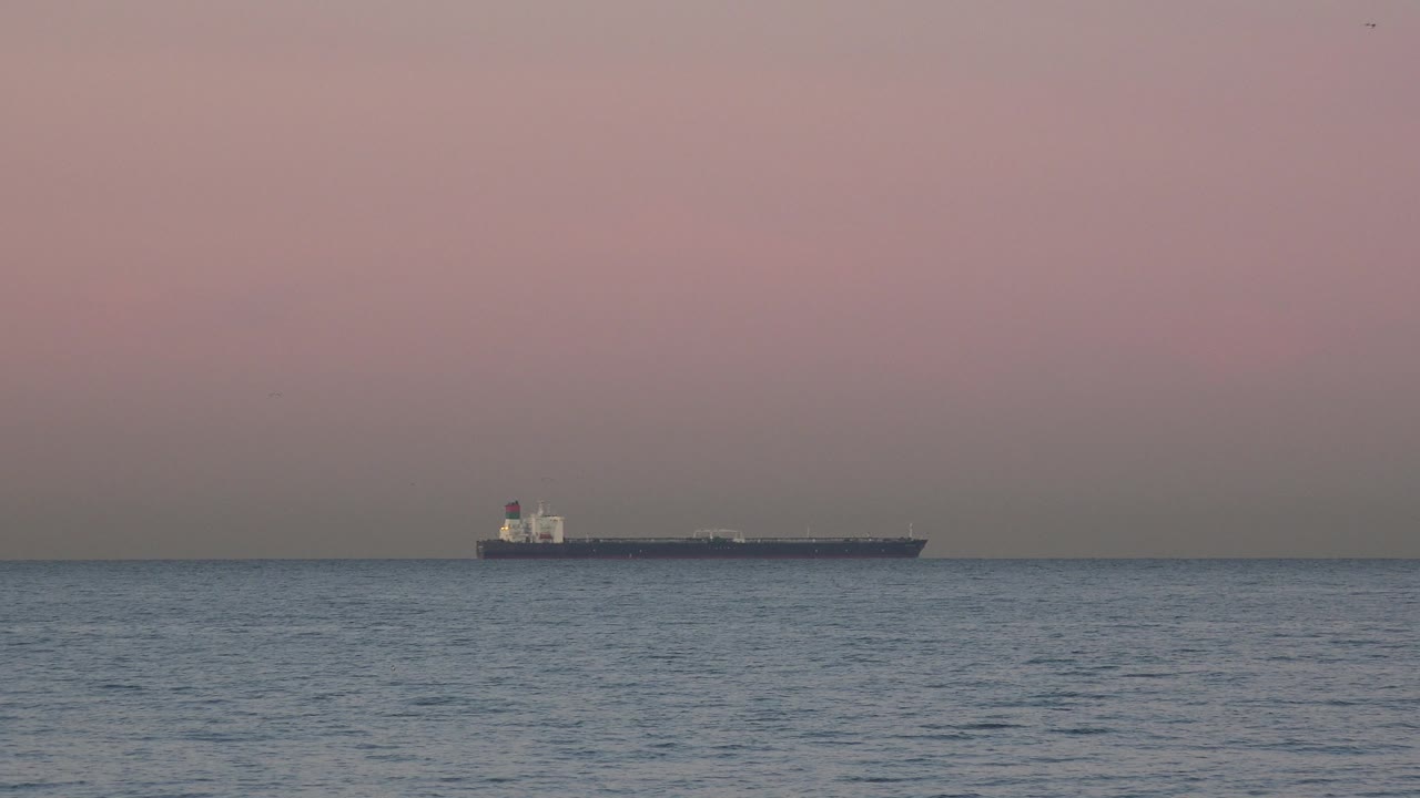 The ship appears near the center of the Huntington Beach horizon, separated from the foreground waves by a broad band of open water and no visible people.