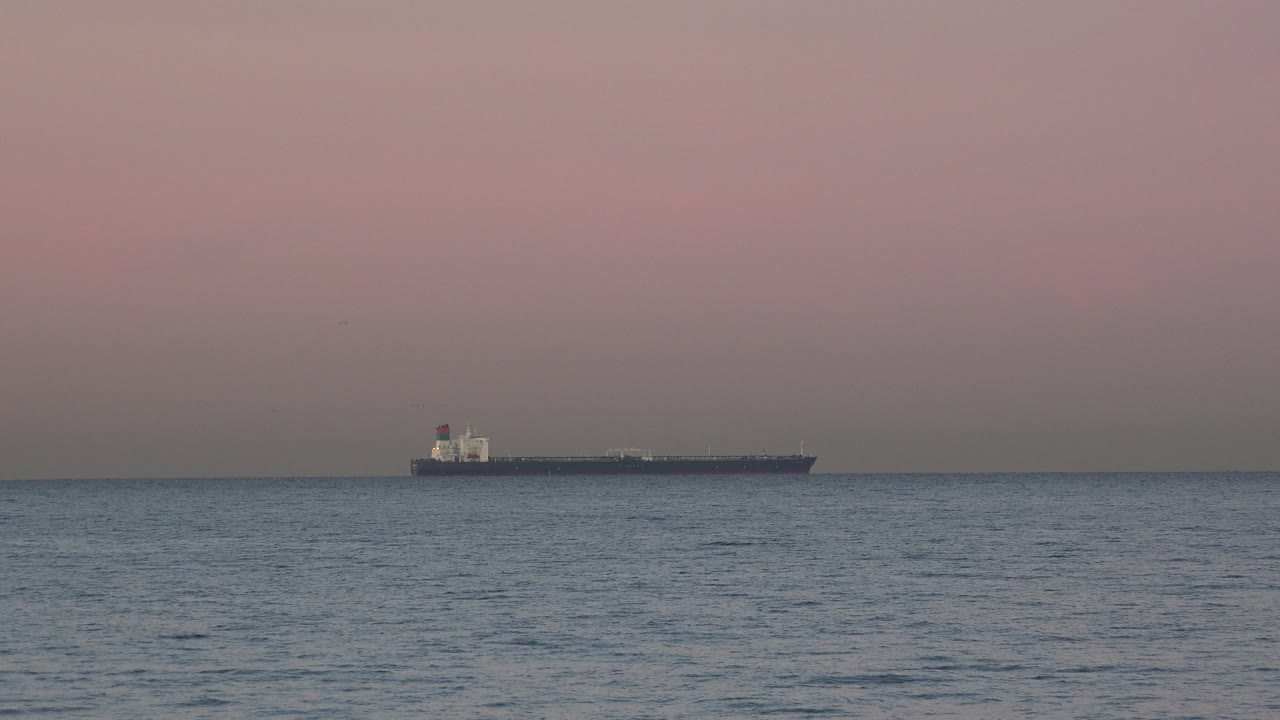 Ship far offshore with darker foreground waves below a pink gray sky.