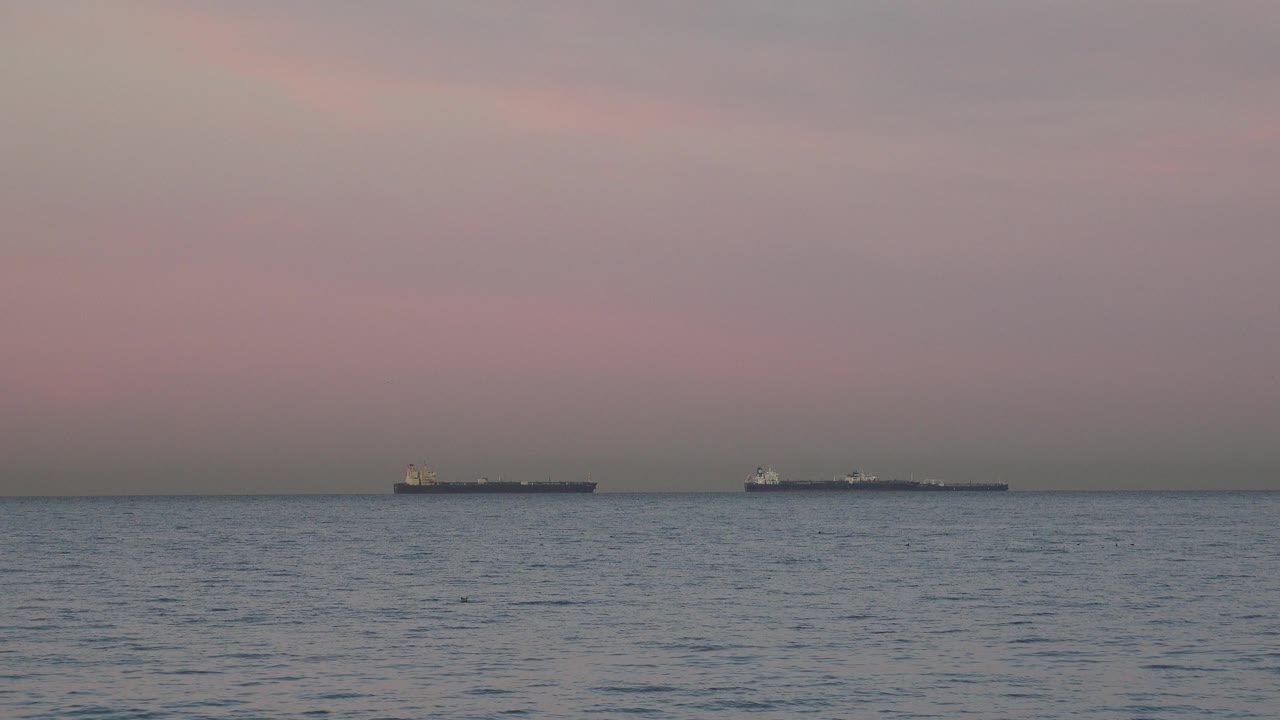 A pair of dark tanker silhouettes remains near the horizon at Huntington Beach, California, above softly rippled water and with no visible people.