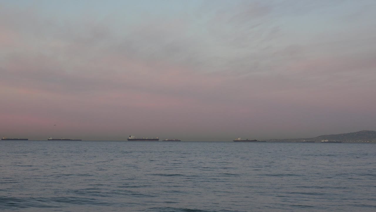 At Huntington Beach, California, anchored tankers appear as dark horizontal shapes across the far horizon while small ripples texture the blue-gray ocean, with no visible people.