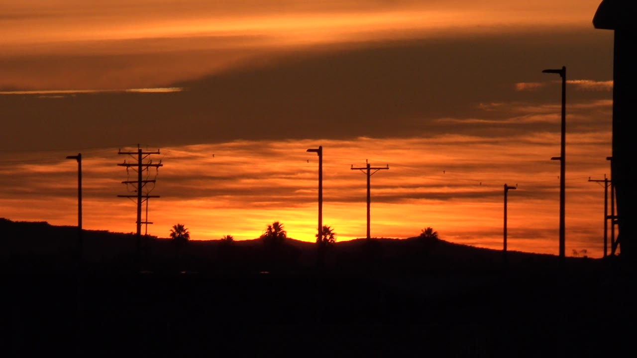 Layered orange clouds over silhouetted roadside poles