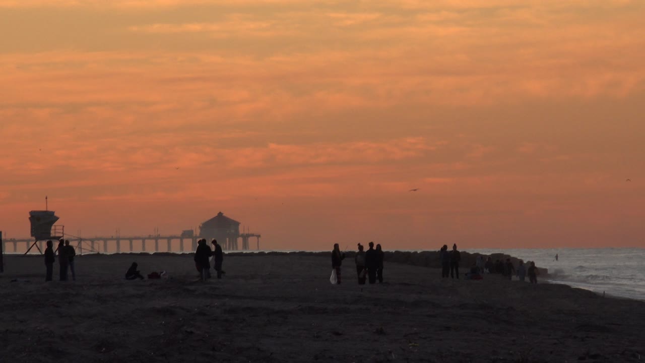 Beach silhouettes with a lifeguard tower and pier under orange clouds.