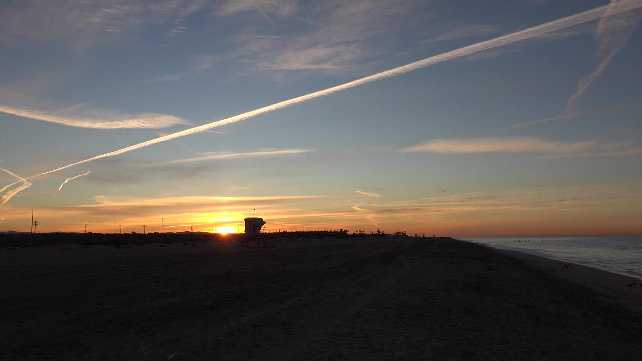 Orange sunset horizon above a shadowed beach and ocean