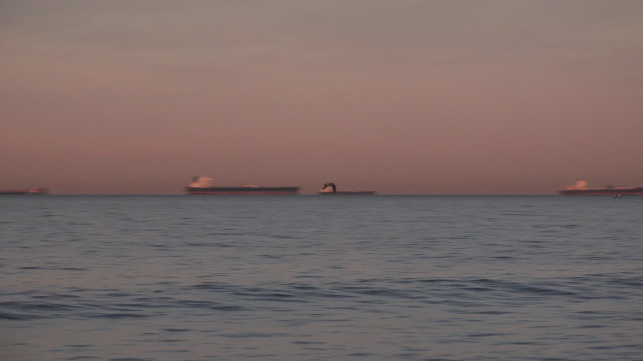 At 0:00 in Huntington Beach, rippled ocean water sits below a pink dusk sky with distant ships on the horizon and no visible people.