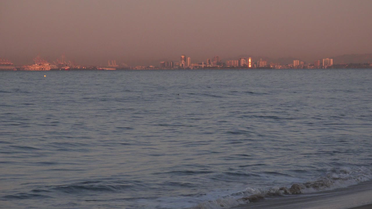 Ocean waves with a distant shoreline under warm haze.