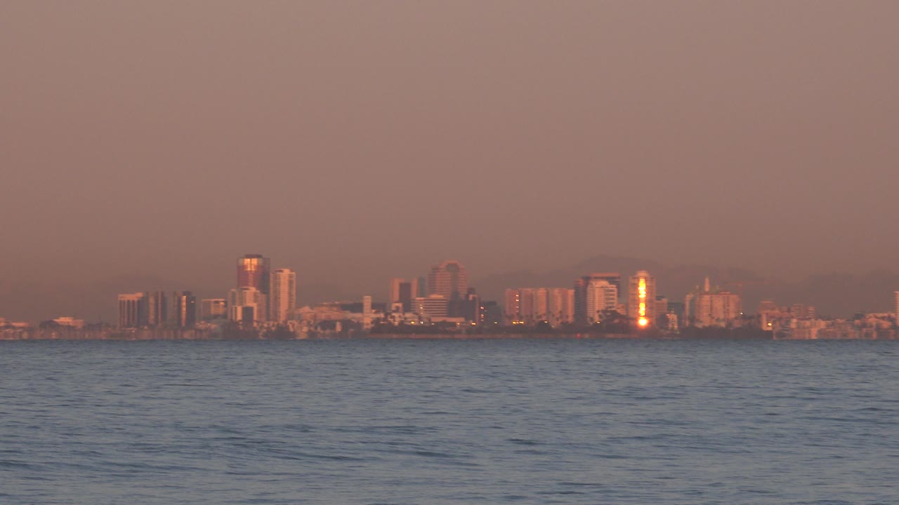 Distant city skyline across rippled ocean at sunset
