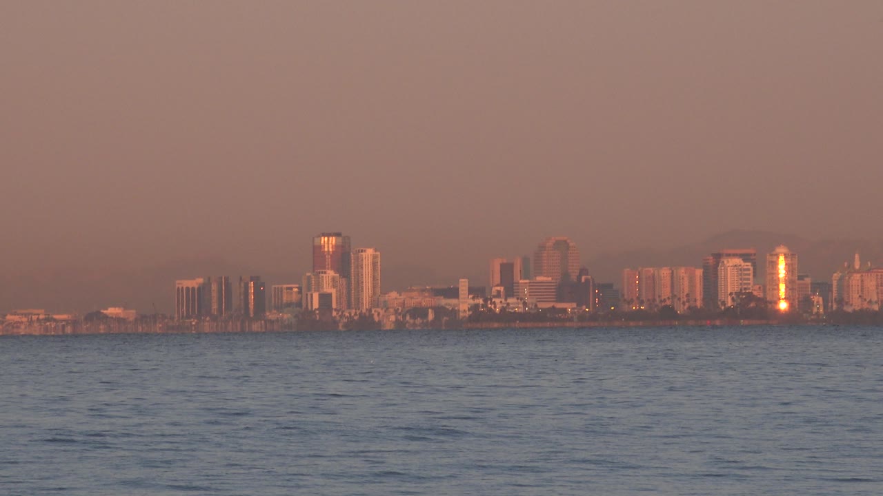 A low band of Huntington Beach buildings catches orange sunset light across the water, with rippled ocean in front and no visible people.