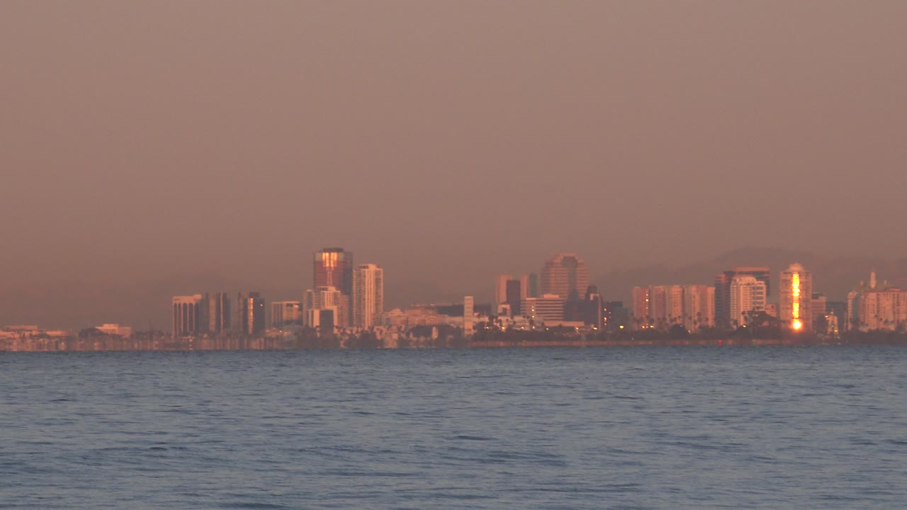 Wide sunset view of city buildings beyond ocean surface