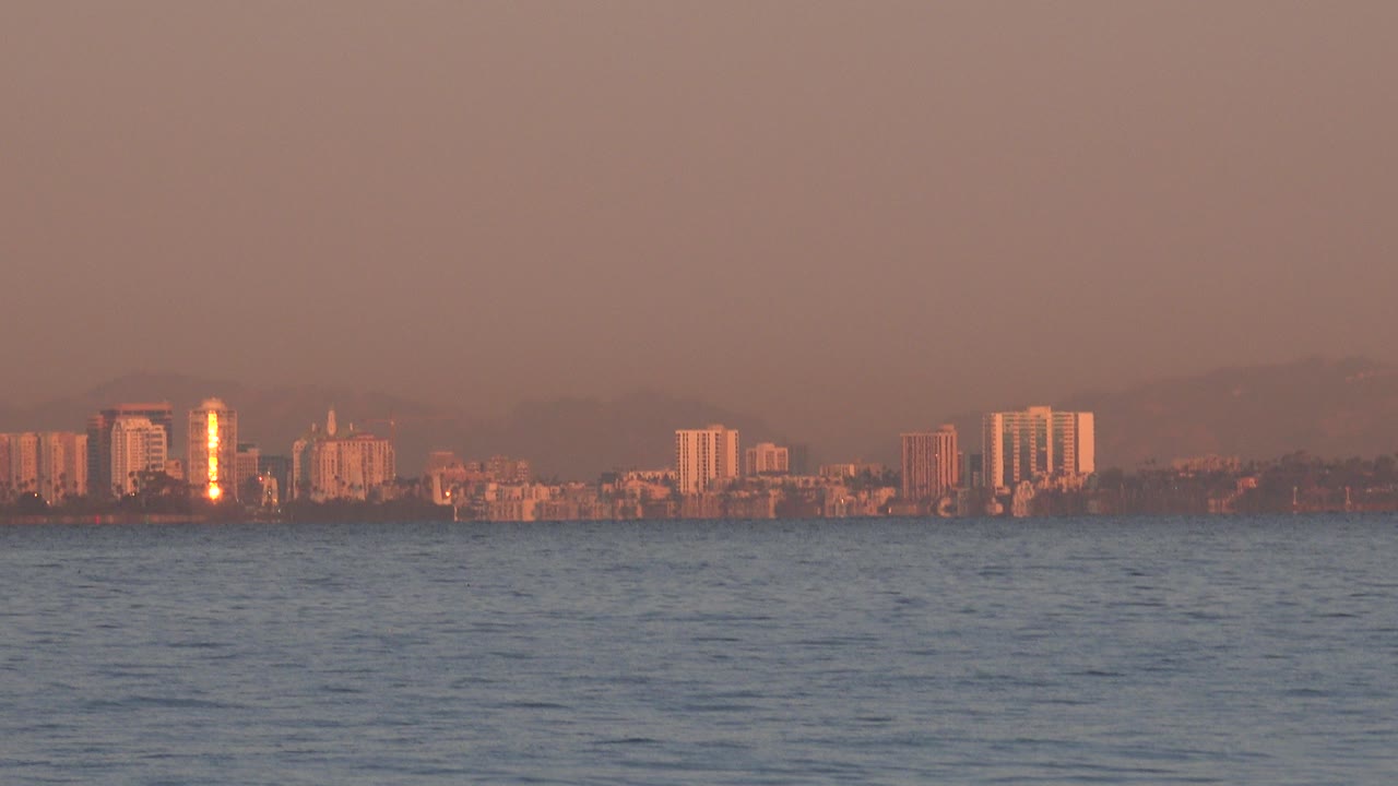 Distant city skyline across ocean water under a warm hazy sky.