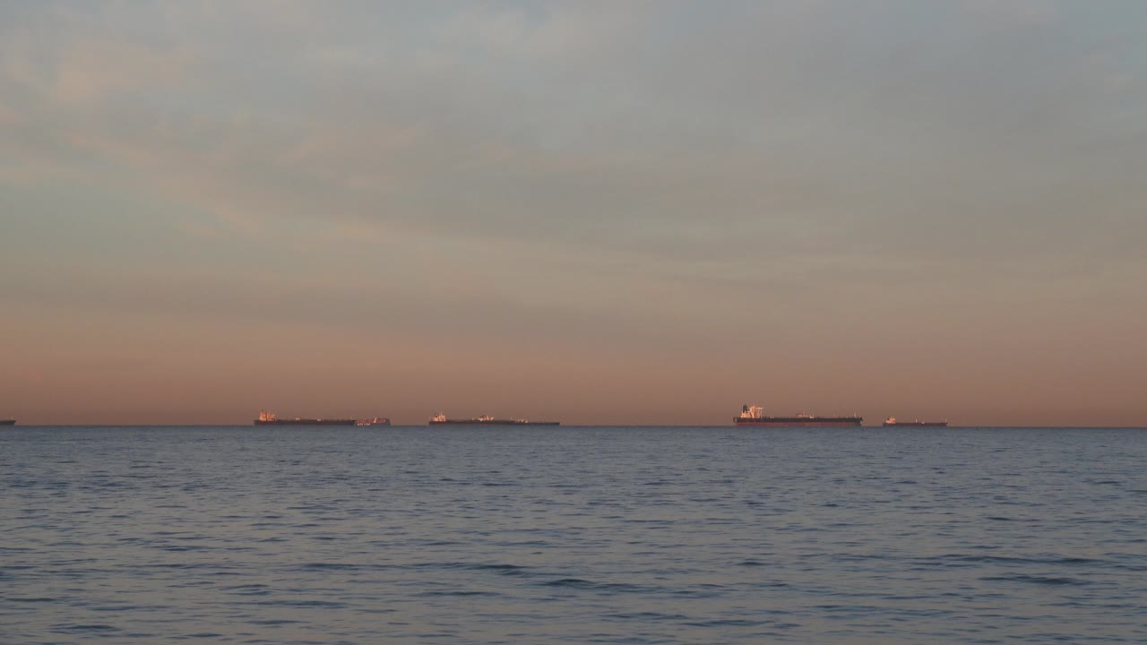 Huntington Beach water fills the lower frame while small ship silhouettes sit on a pink-blue dusk horizon, with no visible people.