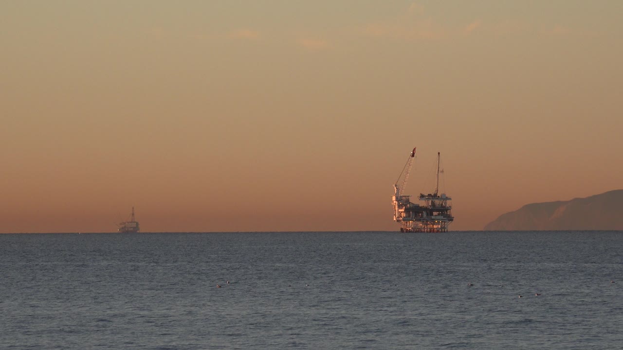 Oil rig and small boat on the ocean at sunset.