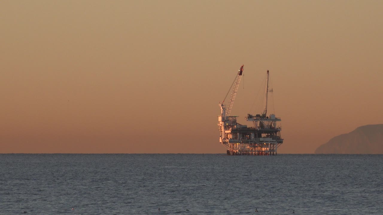 Offshore oil rig at sunset over dark ocean water.