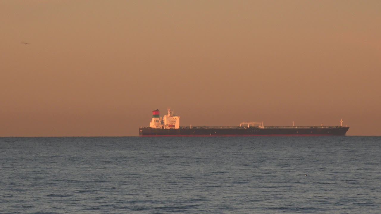 Distant ship on the ocean horizon under an orange evening sky.