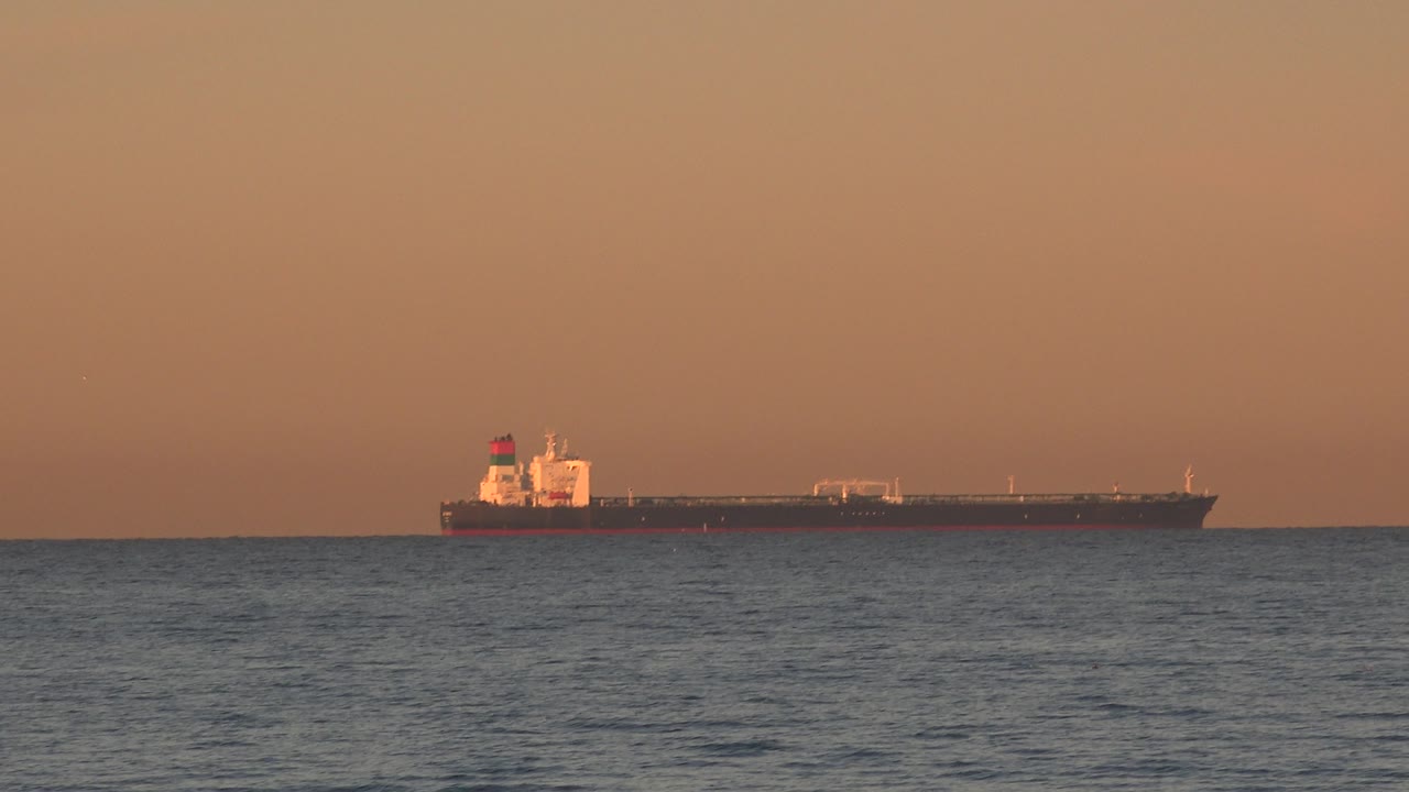 Cargo ship silhouette near the horizon in warm evening light.