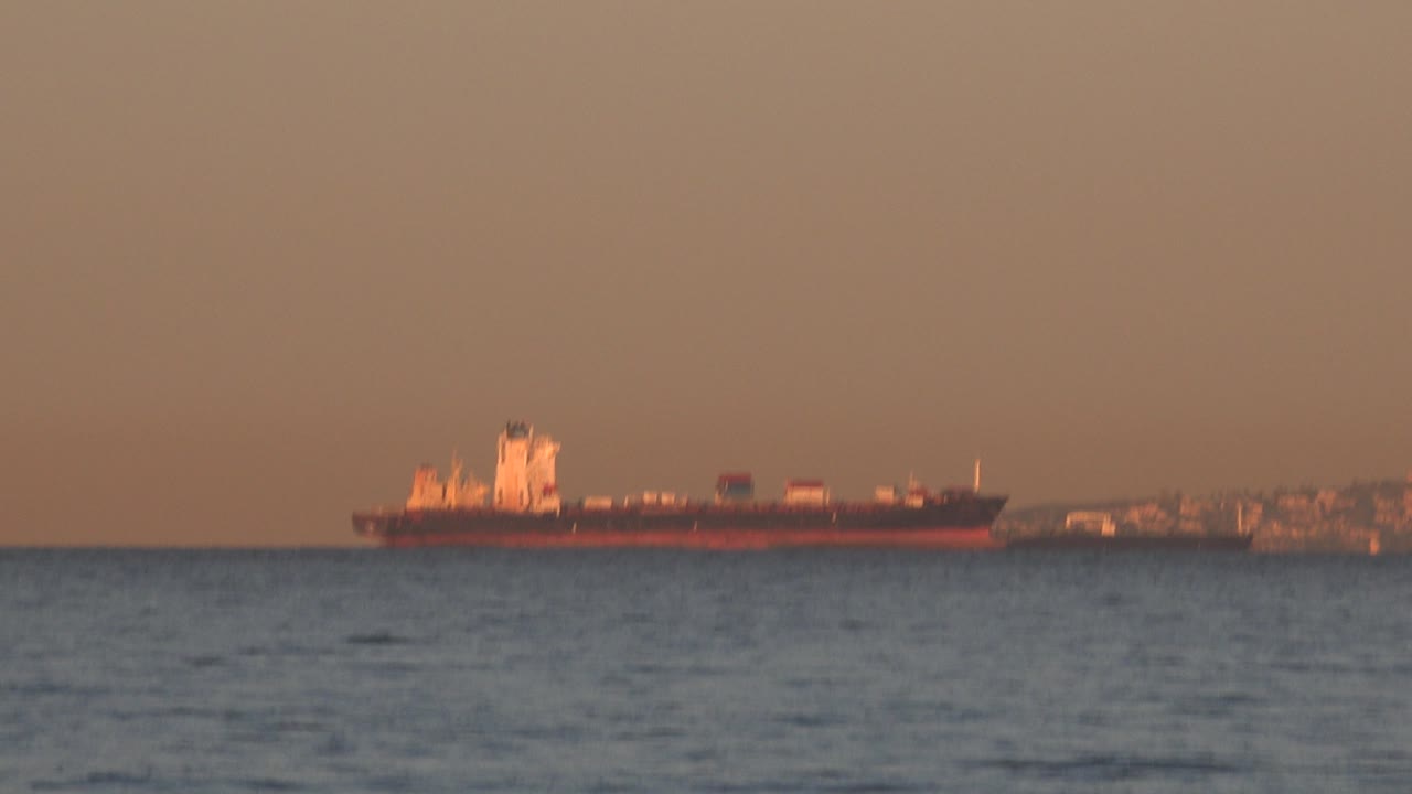 Oil tanker near distant shoreline in orange light.