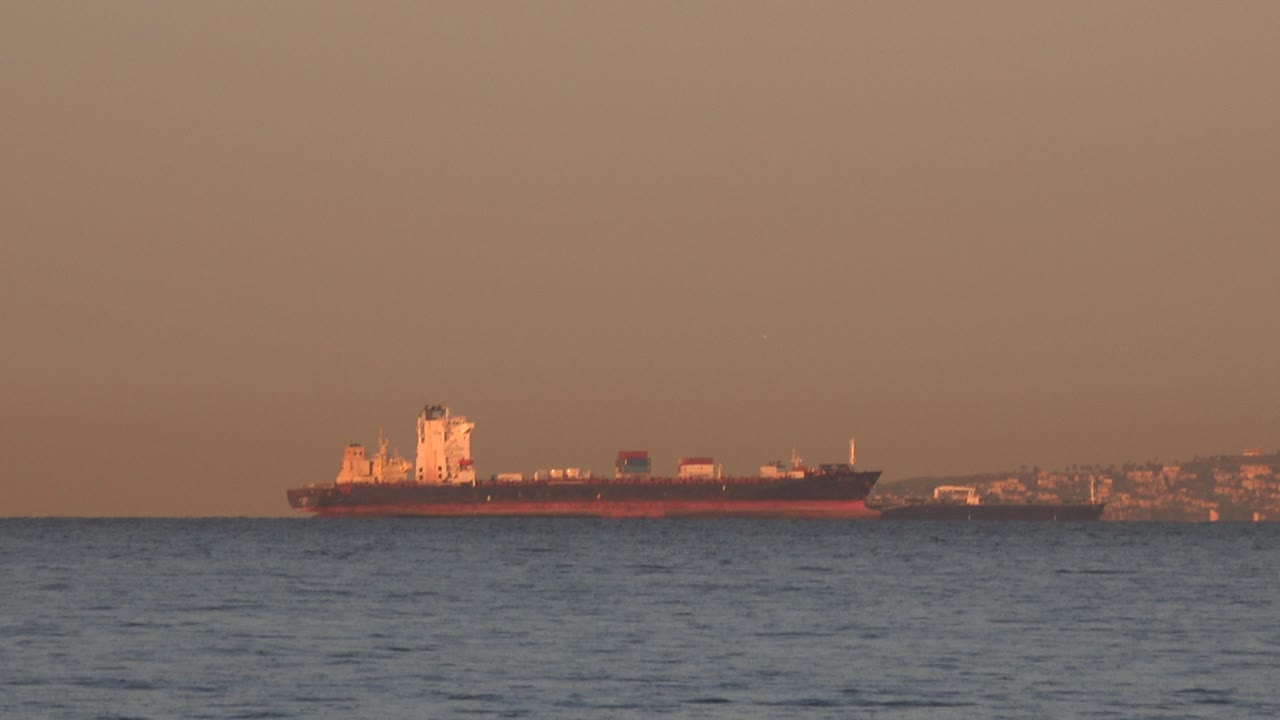 Cargo ship near distant shoreline with orange sky