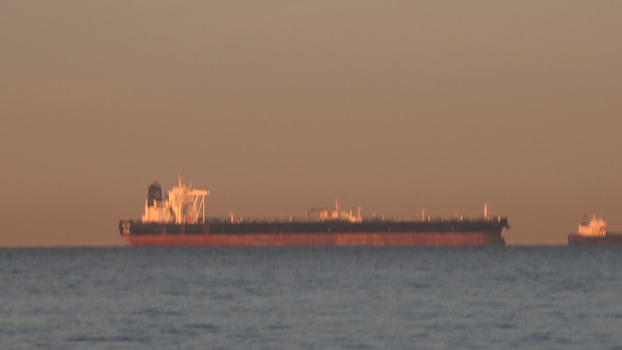 Red and black vessel near horizon with small boat at far right