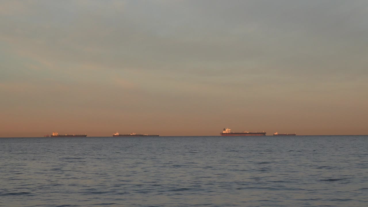 Wide Huntington Beach ocean view with small distant vessels spread across the horizon, rippled water in front, warm low light, and no visible people.