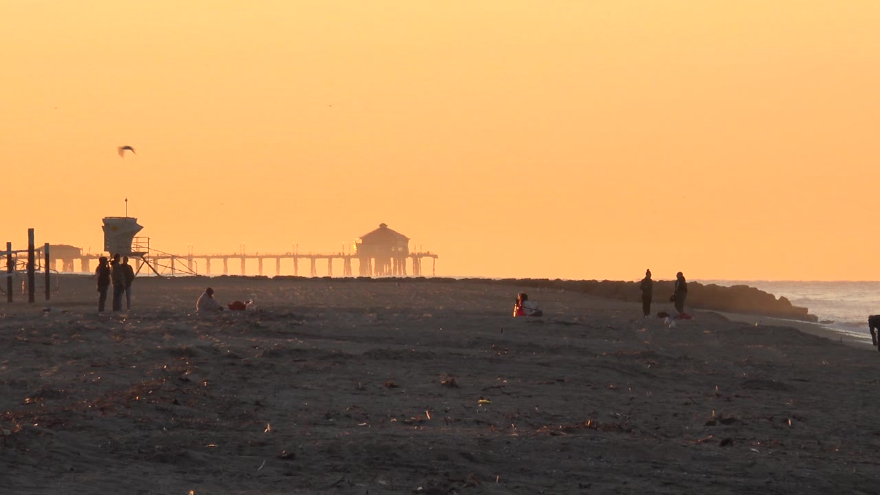 Sparse beach silhouettes with lifeguard tower, pier, and ocean in golden haze.