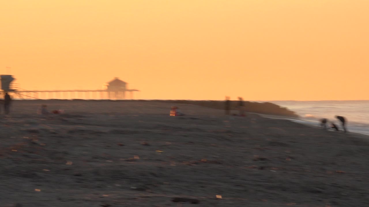 Soft sunset beach frame with pier, ocean, and people near the water.