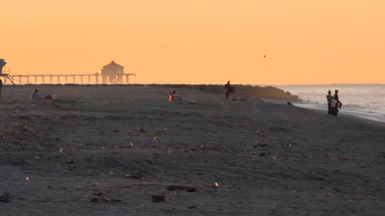 Distant beachgoers and birds on an orange-lit Huntington Beach shoreline.