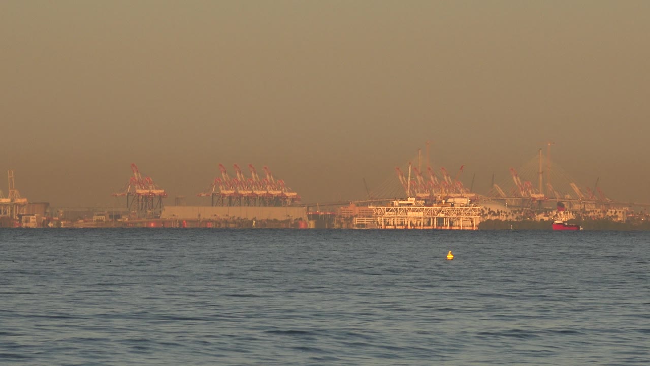 Container port horizon with small red boat and ocean foreground