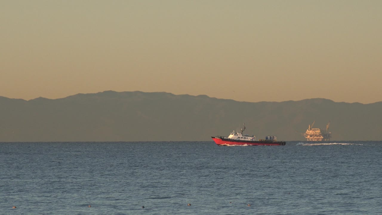 Small red boat near distant offshore structure on calm water.