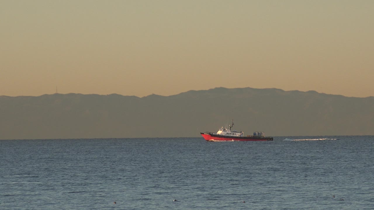 Red boat on ocean with long white wake and mountain horizon.