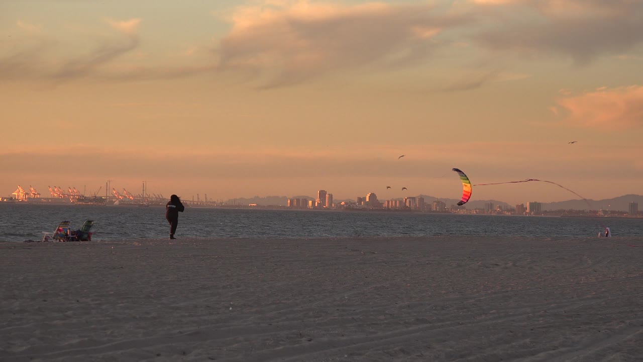 Person walks on the beach while a colorful kite pulls to the right.