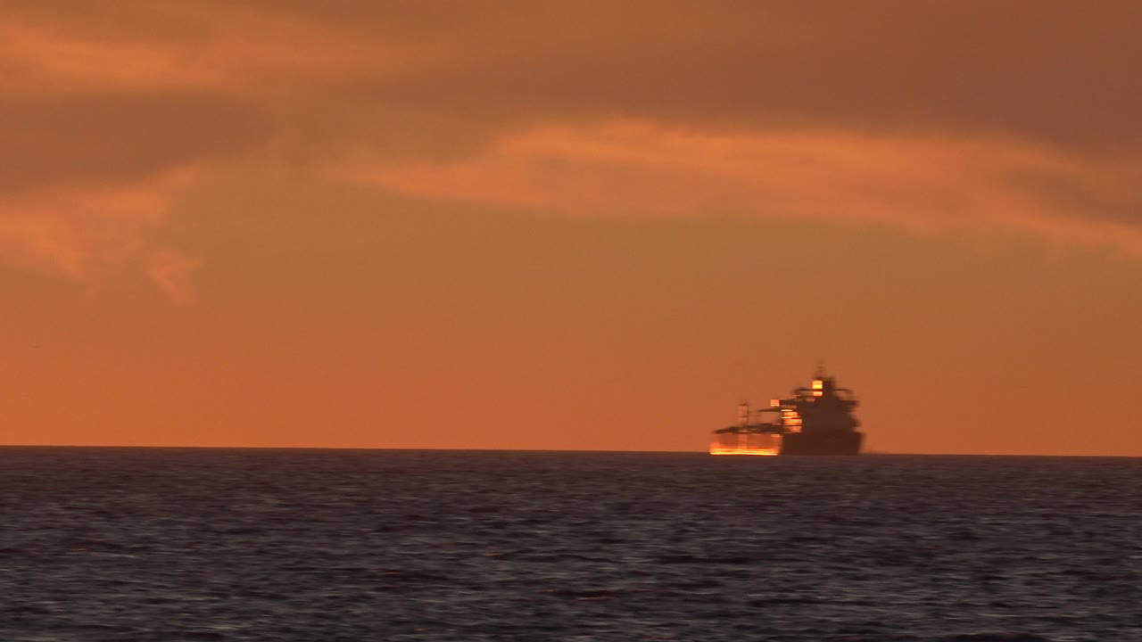 Vessel crossing the distant horizon during sunset.