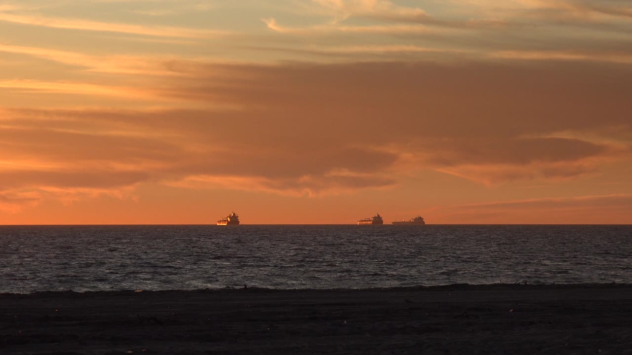 Orange cloud bank above ocean with dark beach foreground.
