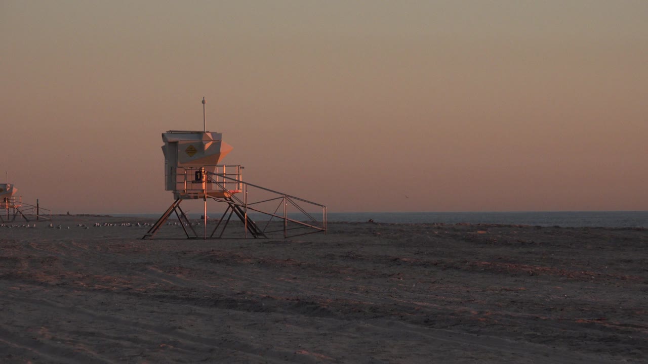 A lifeguard tower sits slightly left of center at Huntington Beach, with railings extending across the sand and the sea line behind it.
