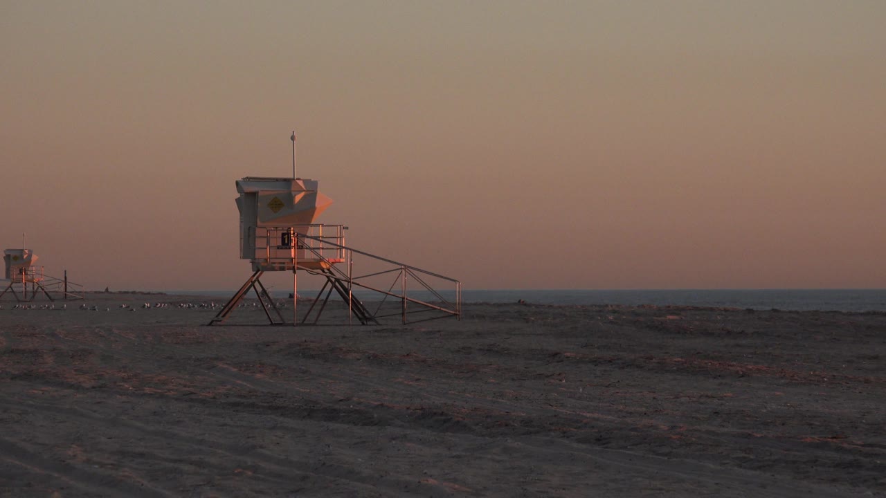 Central lifeguard tower on dark sand with ocean horizon.