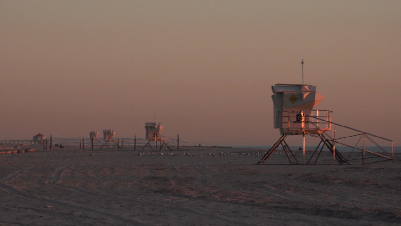Huntington Beach frame with a large raised station on the right, smaller stations receding leftward, flat sand, fencing, and no visible people.