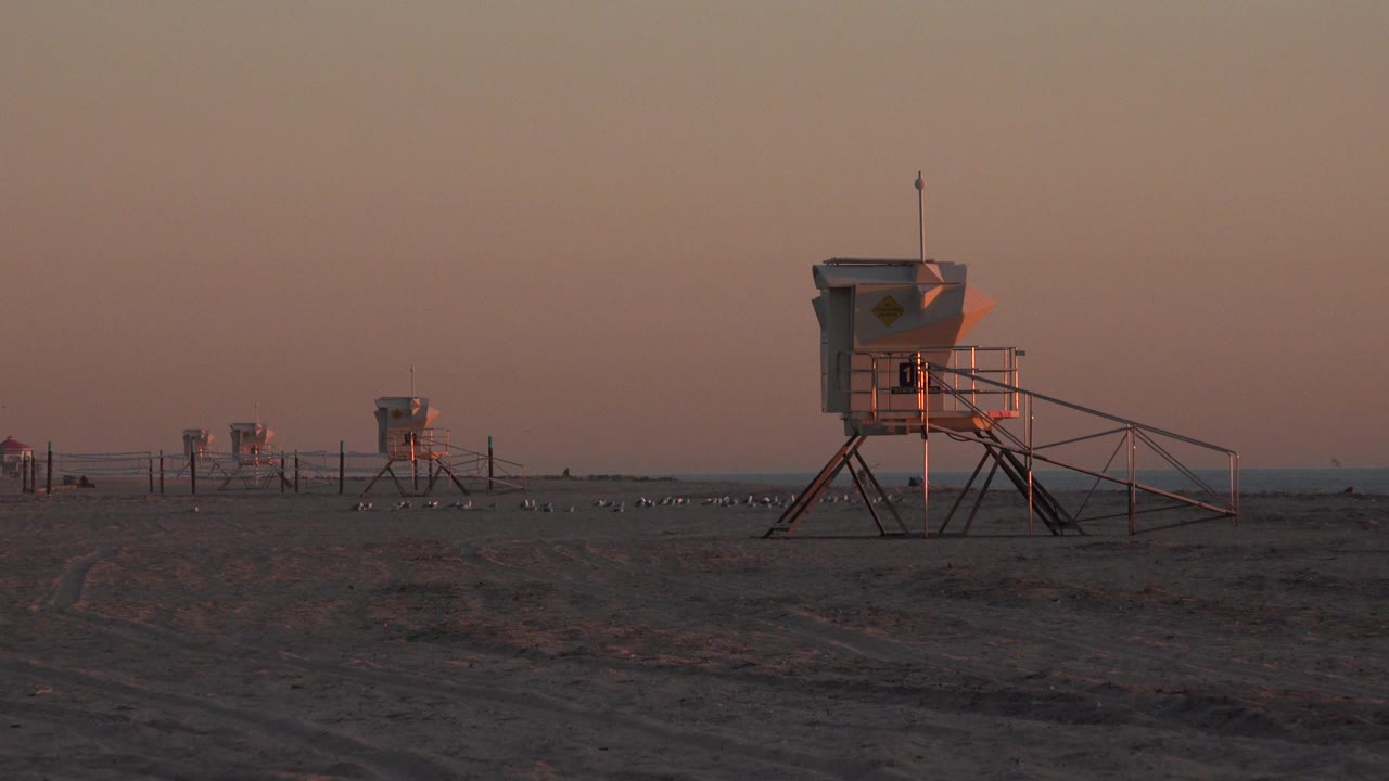 Beach lifeguard stand at dusk with red sky and distant towers.