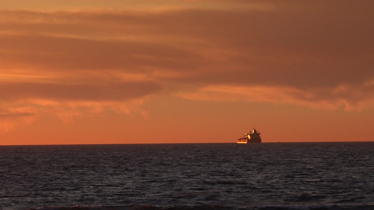 The passenger ship remains near the Huntington Beach horizon as orange light spreads across the sky and the ocean surface darkens below, with no visible people.