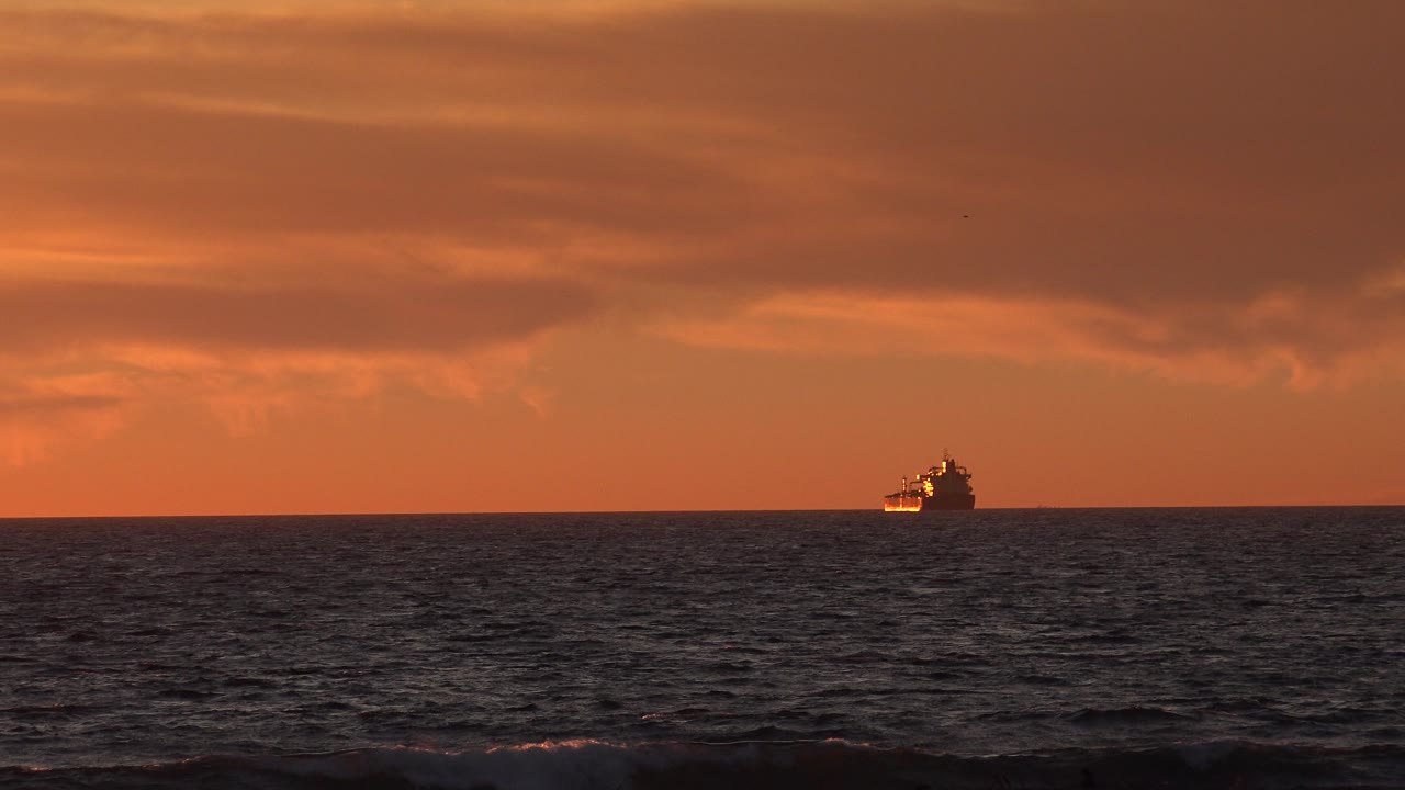 Passenger ship near the right side of the ocean horizon at sunset.