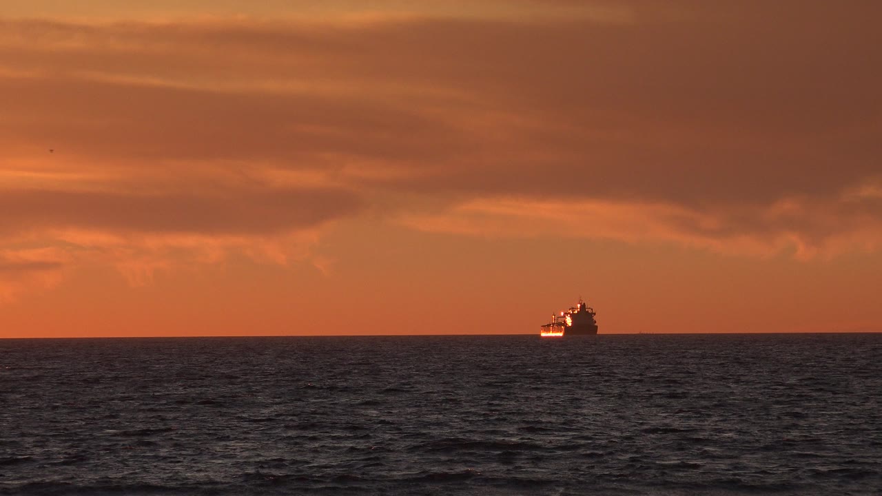 Small boat on the ocean horizon under an orange sunset sky.
