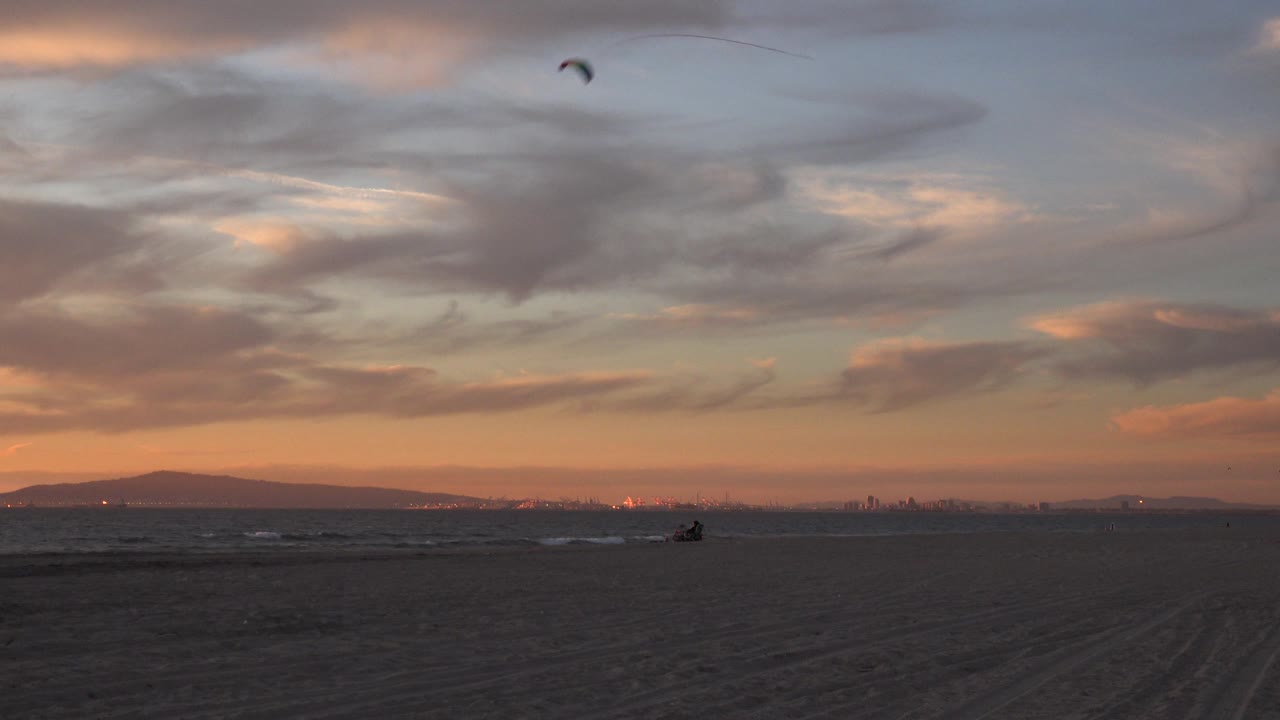 Kite over broad sunset clouds with beach and ocean below.