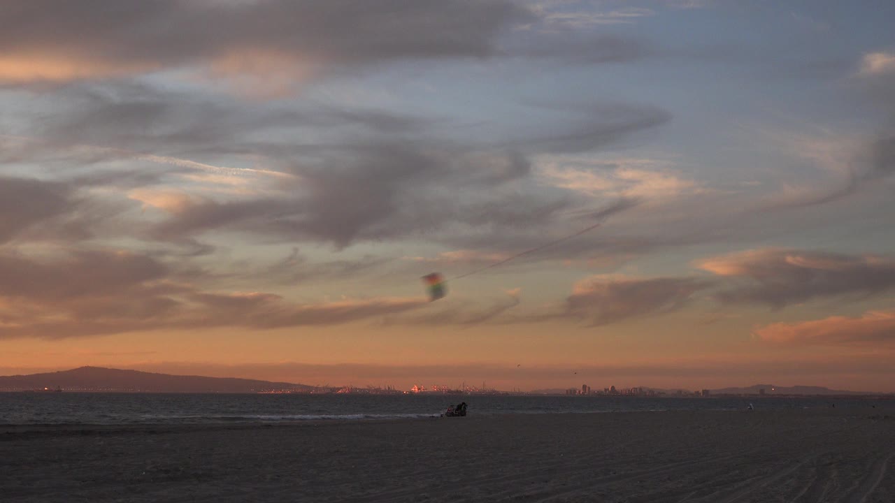 Small red kite over a dark beach and distant ocean horizon at dusk.