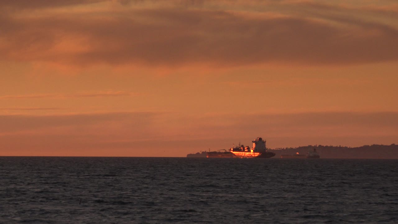 Distant ship and shoreline beneath orange cloud layers