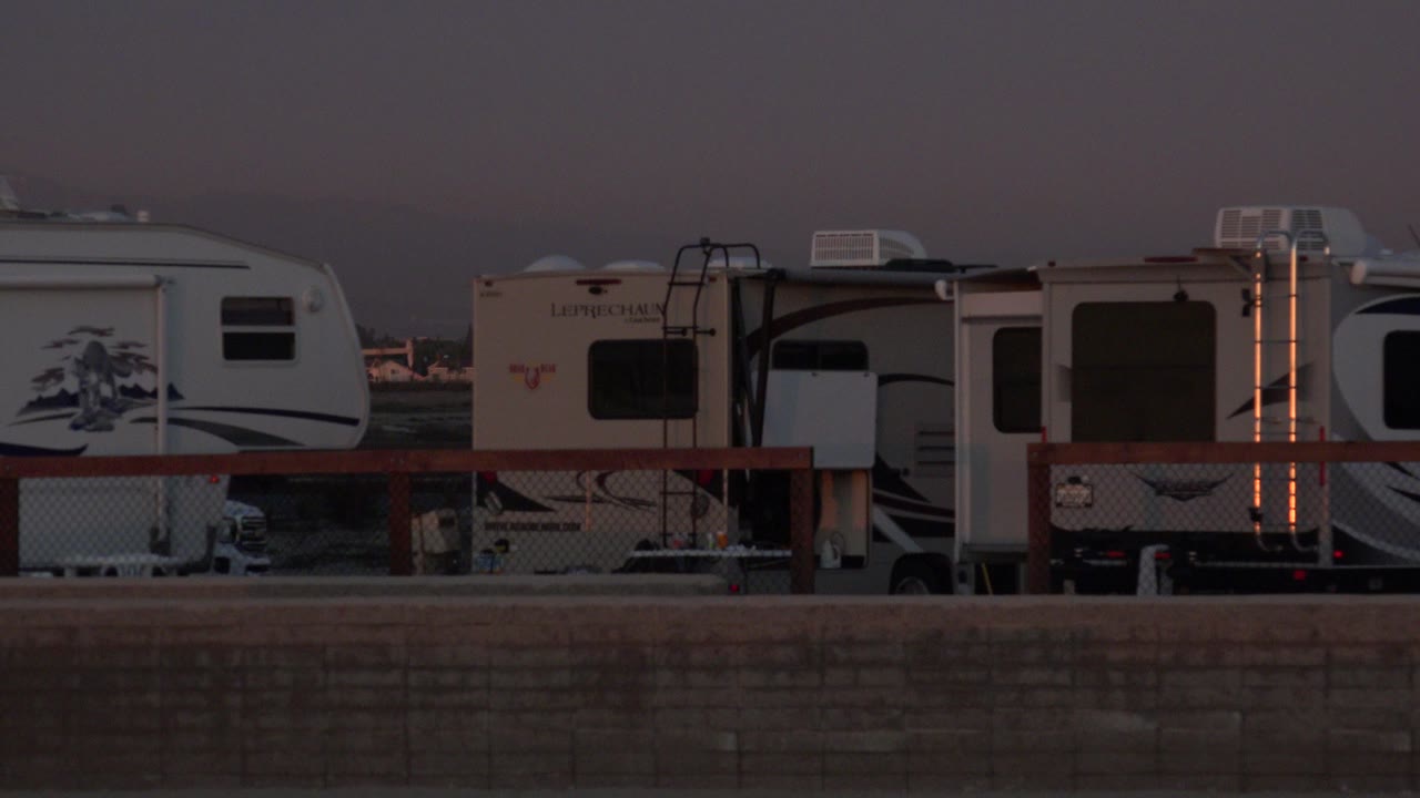 Camping vans parked behind a low roadside wall at dim light.